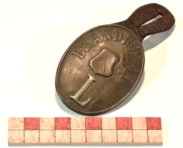 878259 Afbeelding van een koperen insigne van de Utrechtse Vrijwillige Brandweer, met de tekst 'BRANDWEZEN', een ...